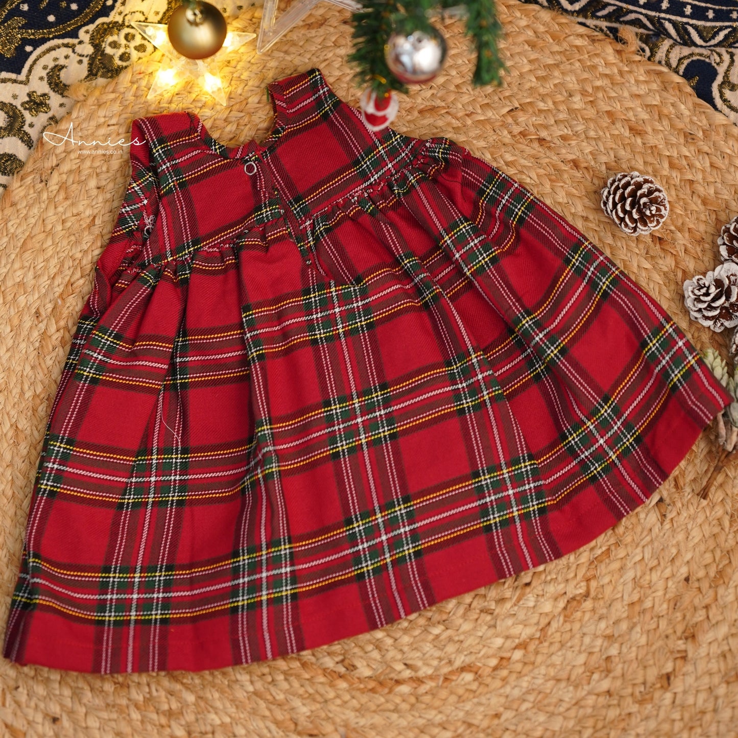 Red plaid dress on a woven surface with Christmas decorations.