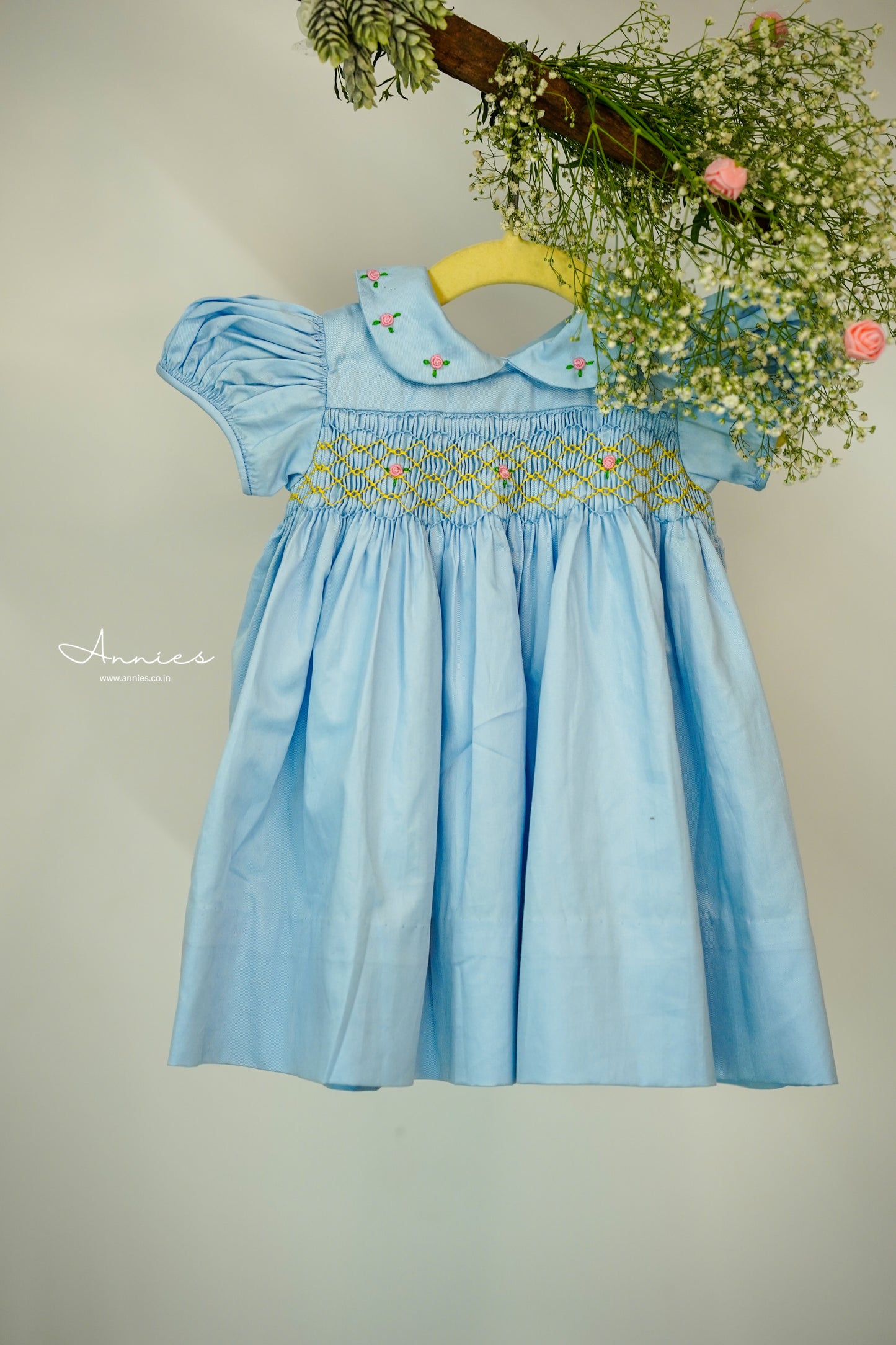Light blue dress with floral embroidery on a hanger against a neutral background