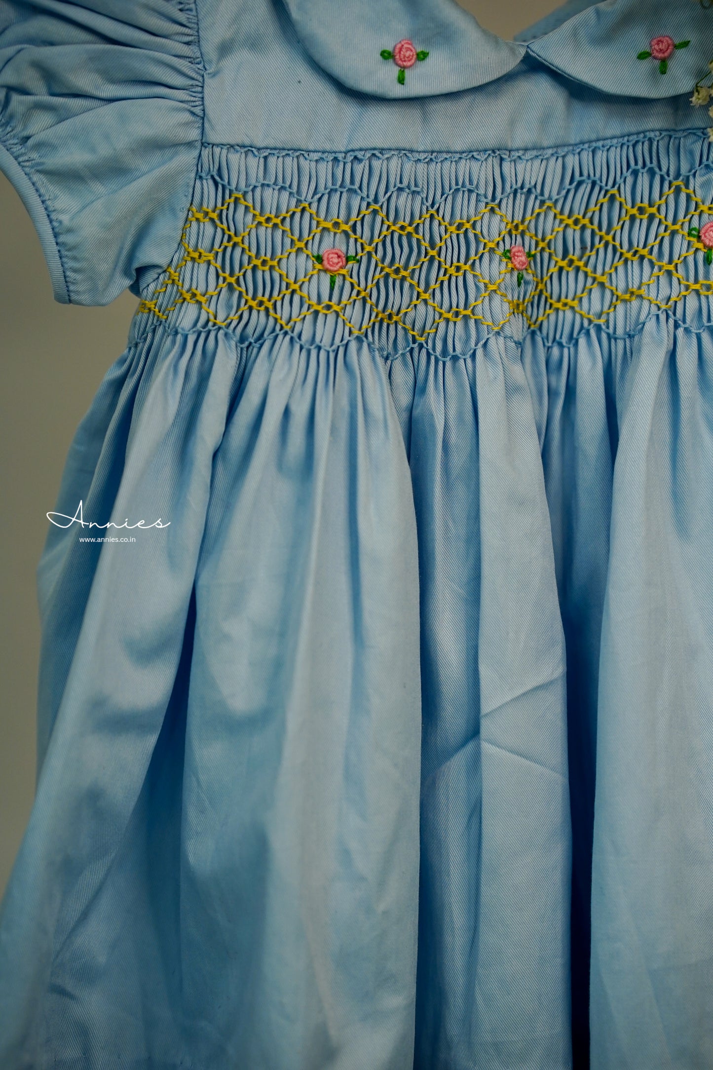 Light blue dress with smocked waist and floral embroidery on a plain background