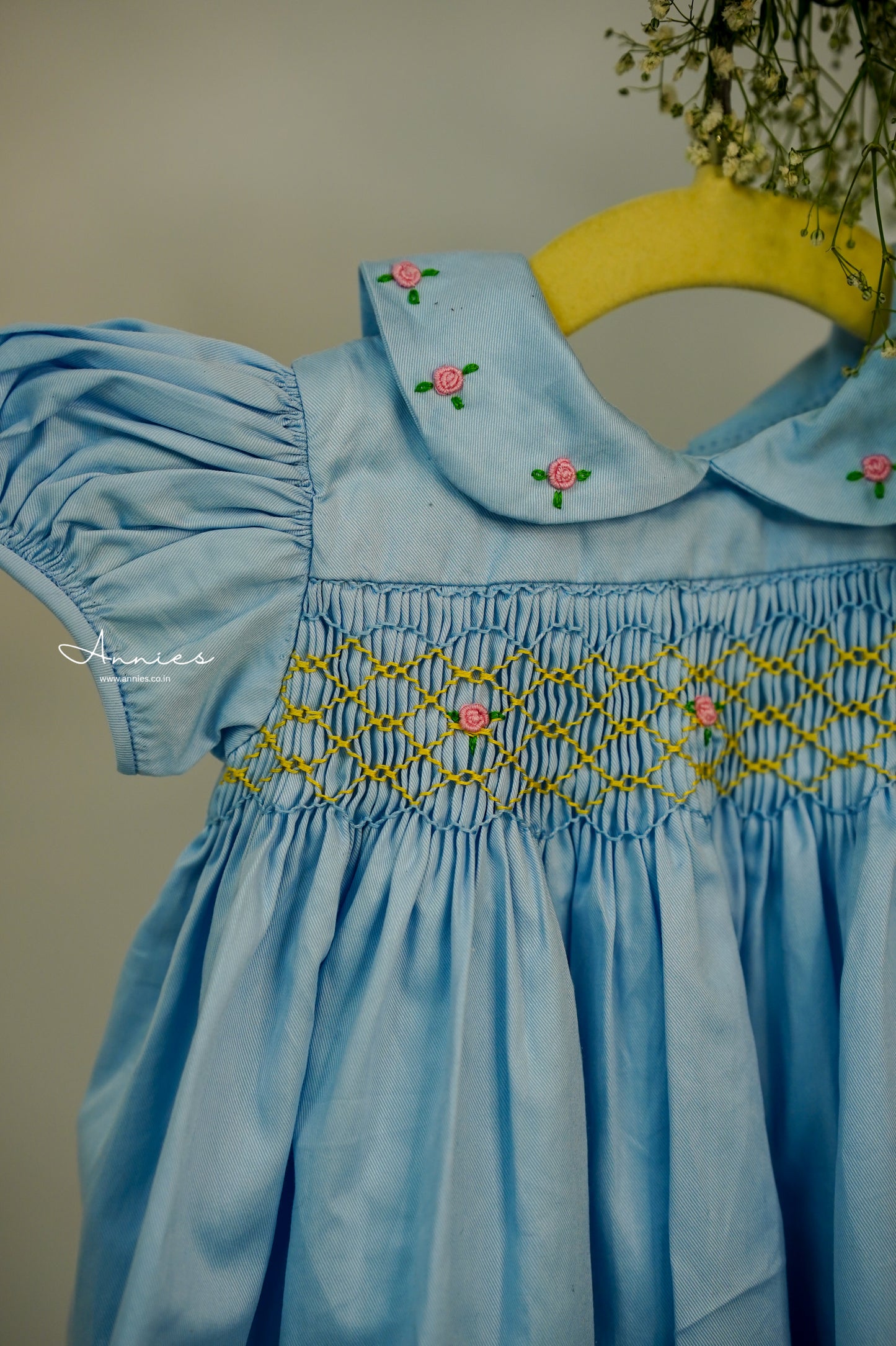 Light blue dress with floral embroidery on a yellow hanger against a neutral background