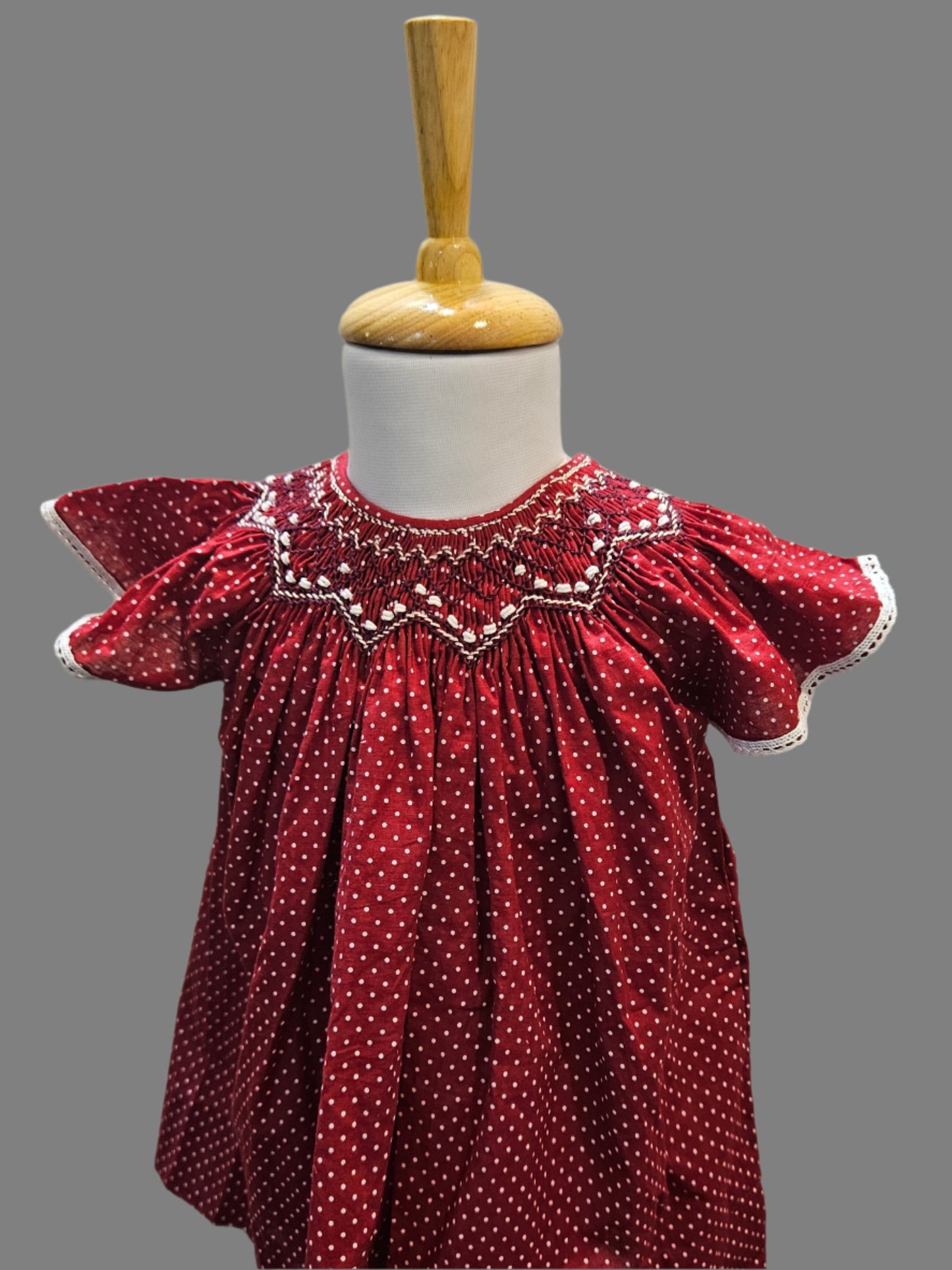 Front view of a handmade maroon smocked bishop dress for babies with flutter sleeves and intricate embellishments, displayed on a mannequin.