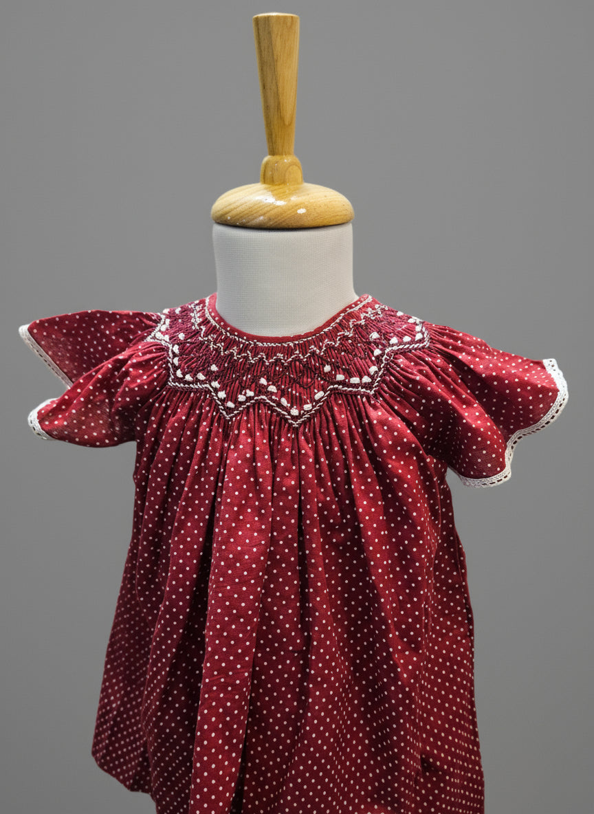 Front view of a handmade maroon smocked bishop dress for babies with flutter sleeves and intricate embellishments, displayed on a mannequin.