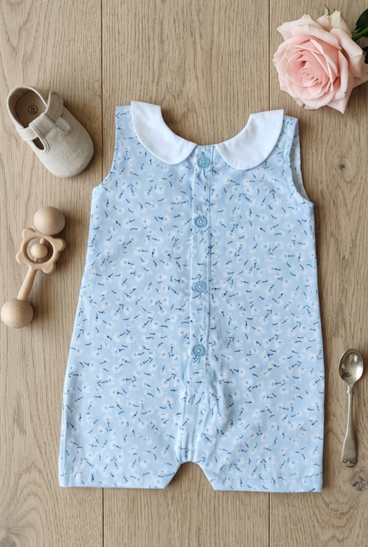 Baby romper with floral pattern on a wooden surface with toys and a rose.
