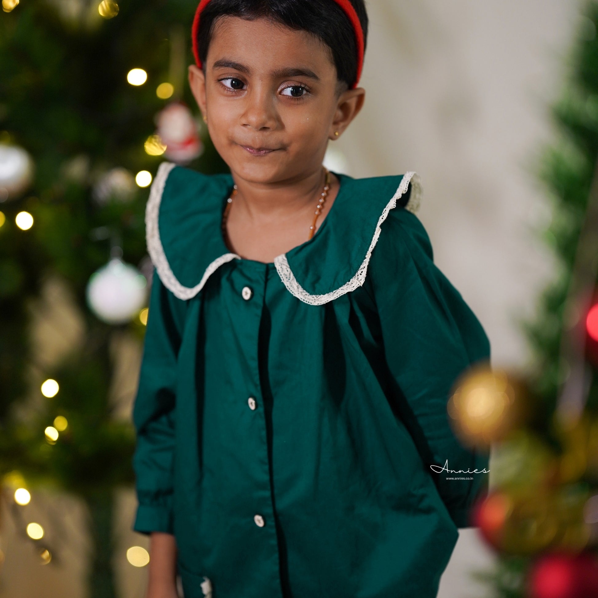 Child wearing a green dress with a blurred Christmas tree background