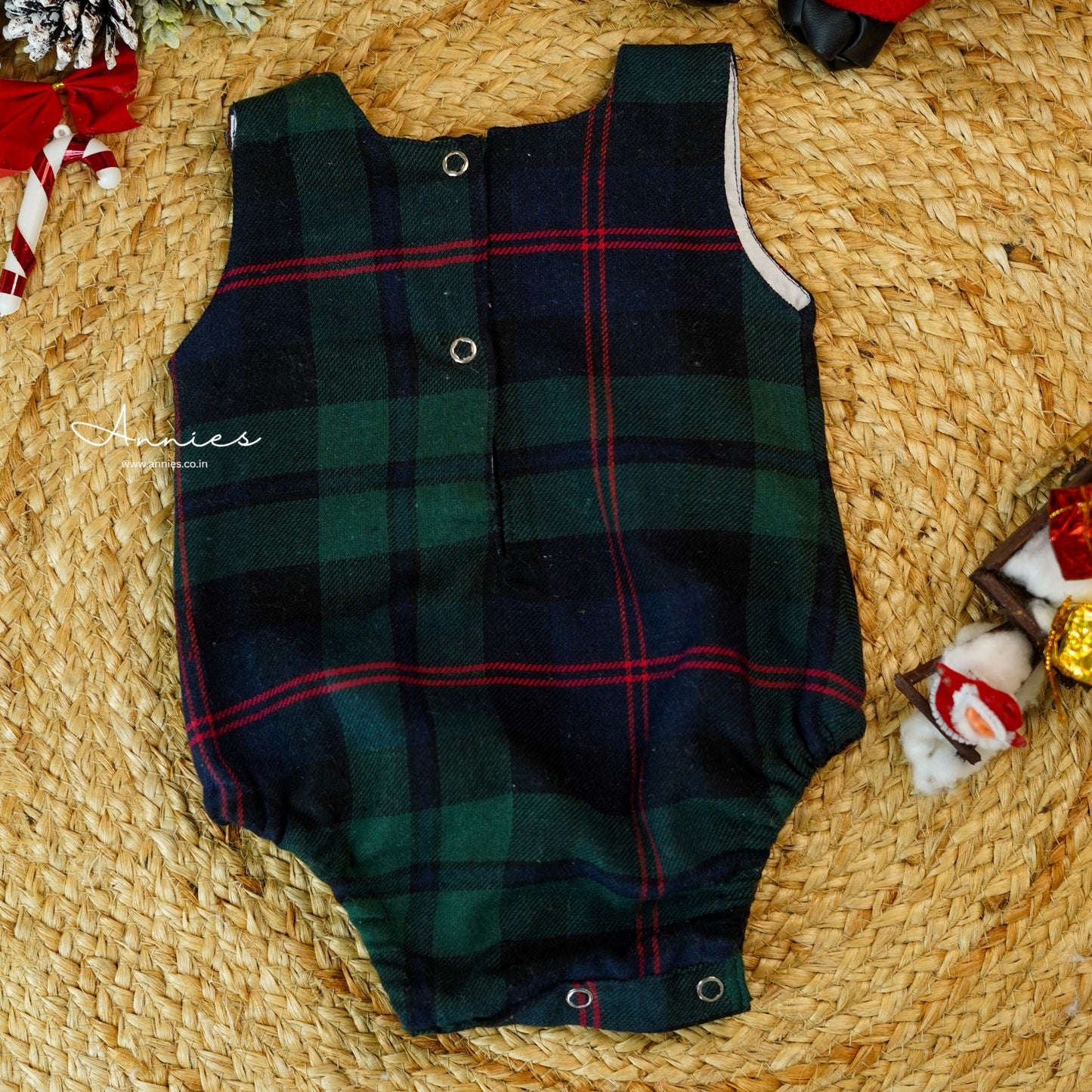 Green plaid baby romper on a woven surface