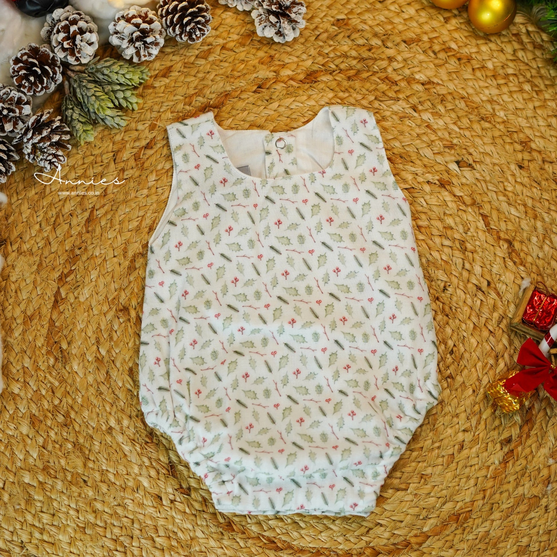 Baby romper with floral pattern on a woven surface with pinecones and a red bow.