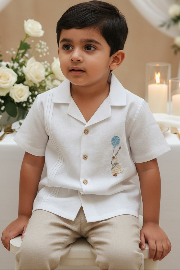Young boy in a white shirt with embroidered design sitting in a decorated room.