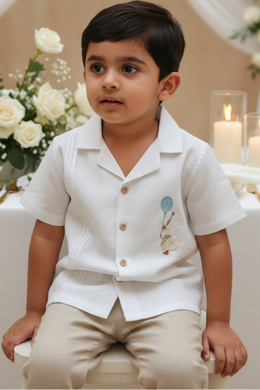 Young boy in a white shirt with embroidered design sitting in a decorated room.