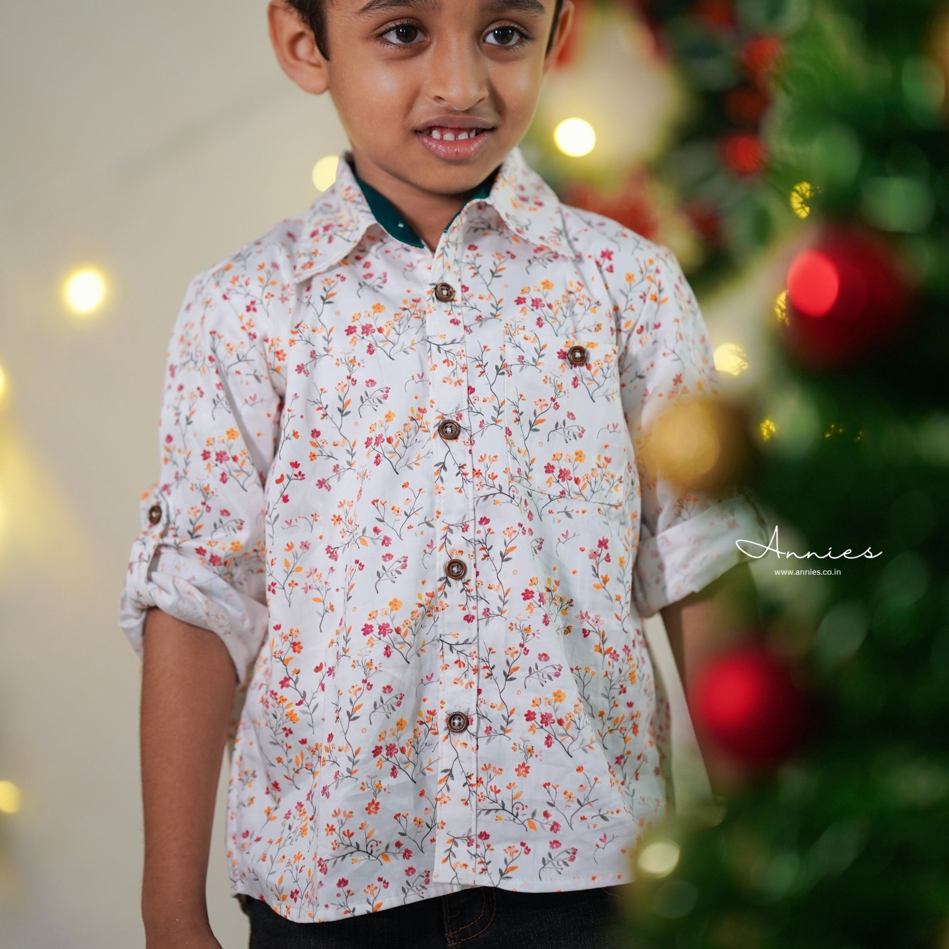 Child wearing a floral shirt with a blurred Christmas tree in the background