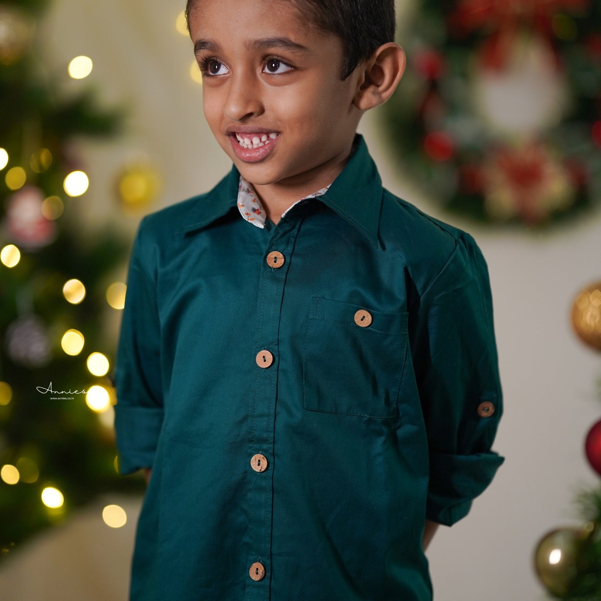 Young boy in a green shirt standing in front of a decorated Christmas tree.