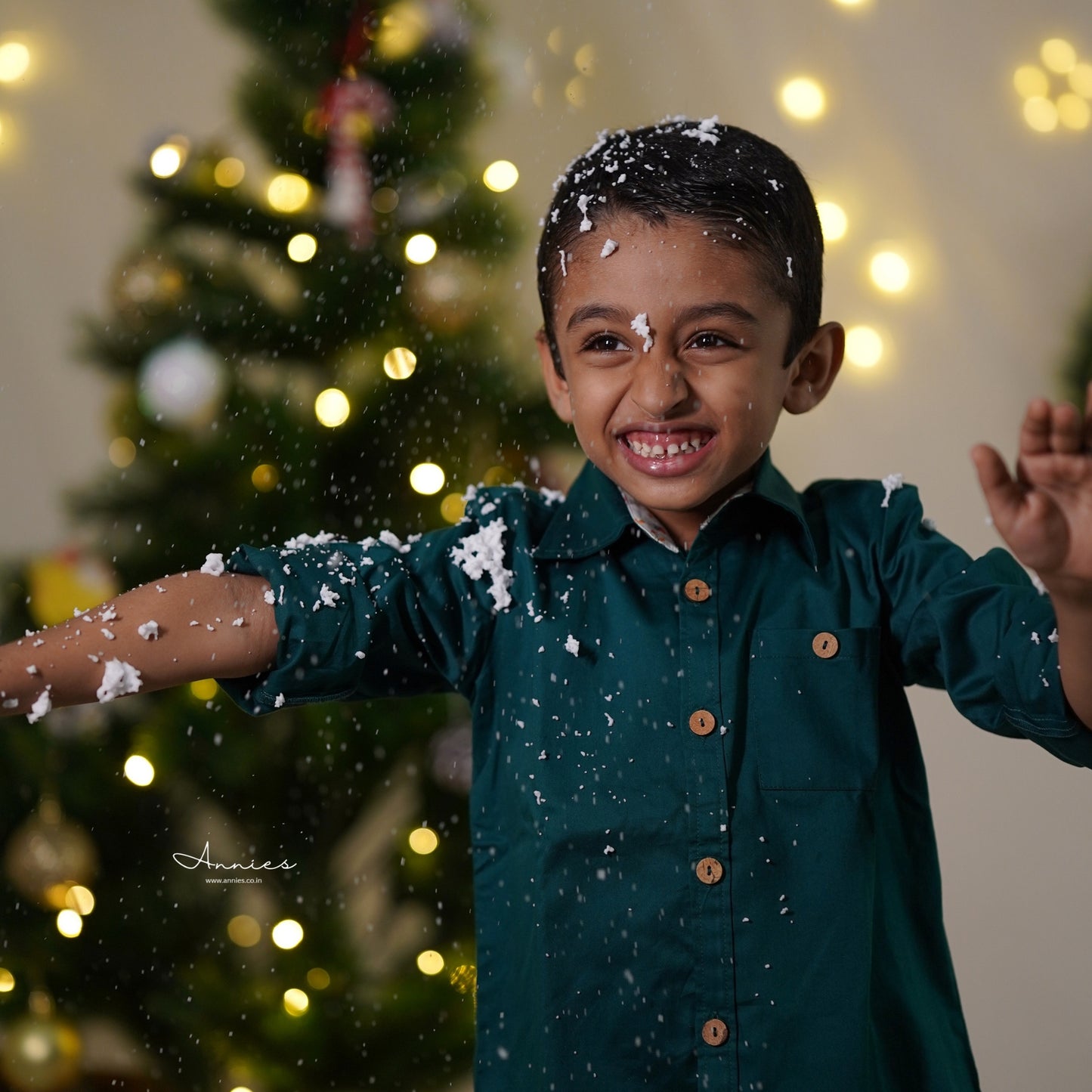 Child in a green shirt with snowflakes around, Christmas tree in the background