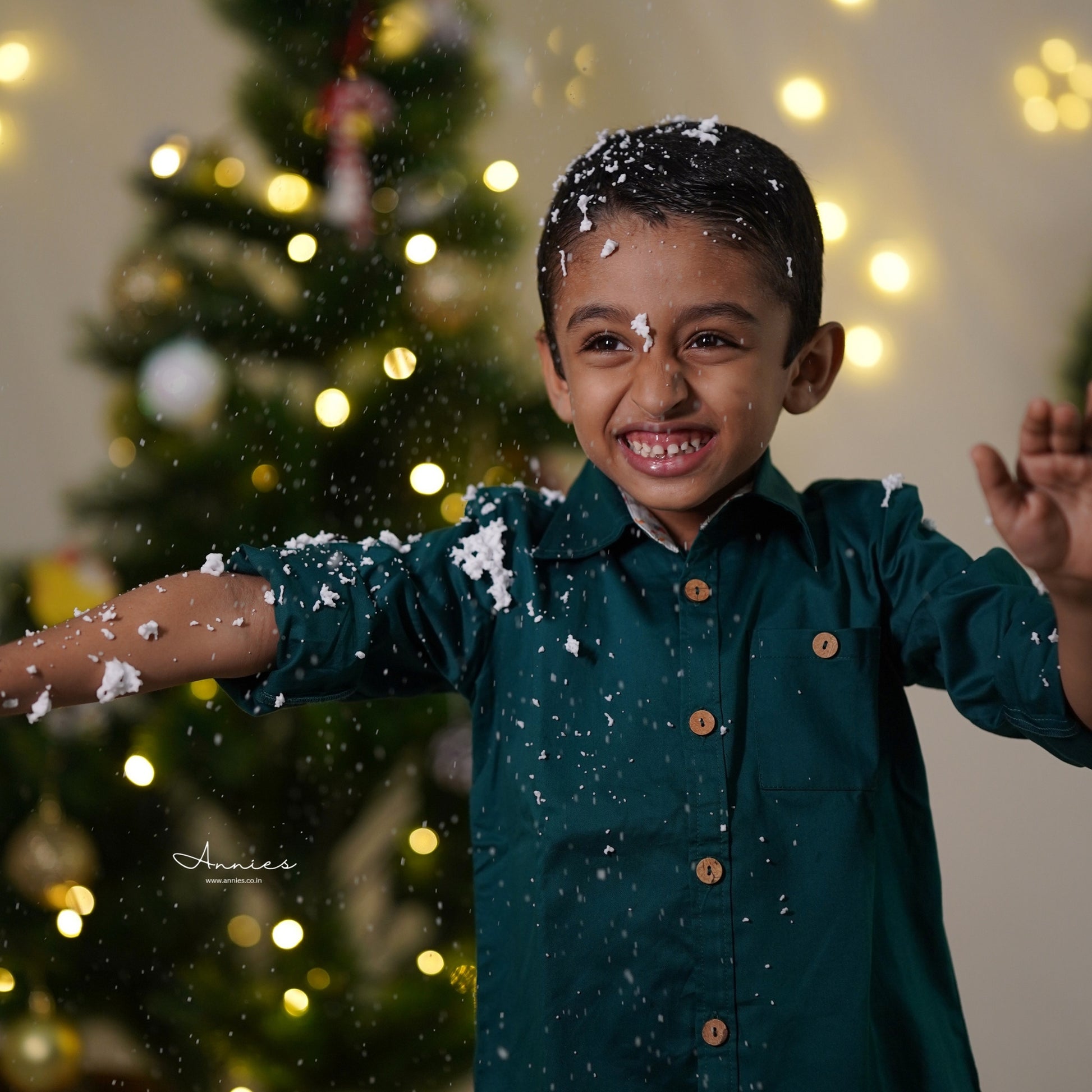 Child in a green shirt with snowflakes around, Christmas tree in the background