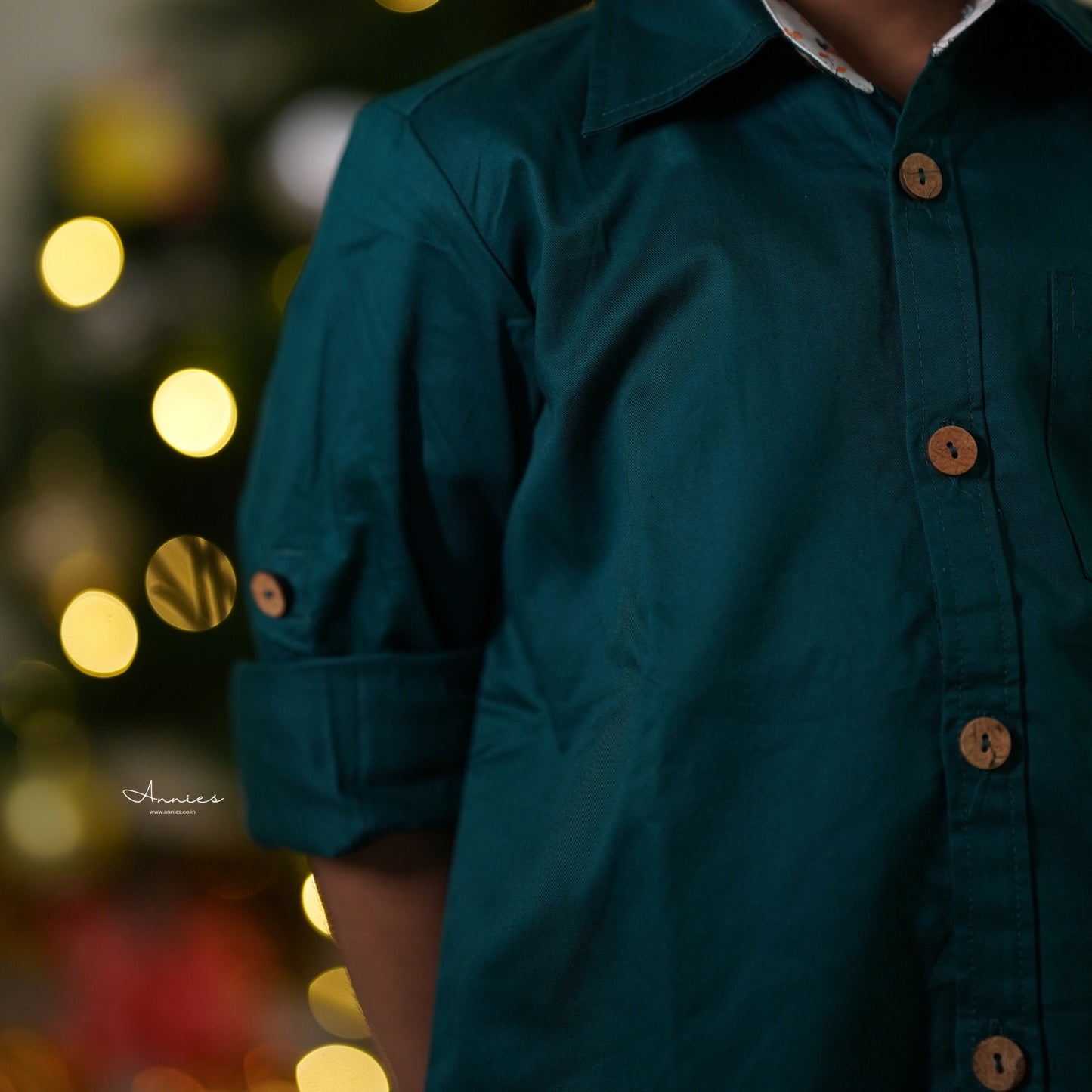 Boy wearing a green shirt with wooden buttons against a blurred festive background with lights.