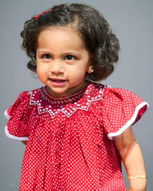 A girl wearing adorable handmade maroon smocked bishop dress for babies with flutter sleeves and delicate embellishments, perfect for special occasions