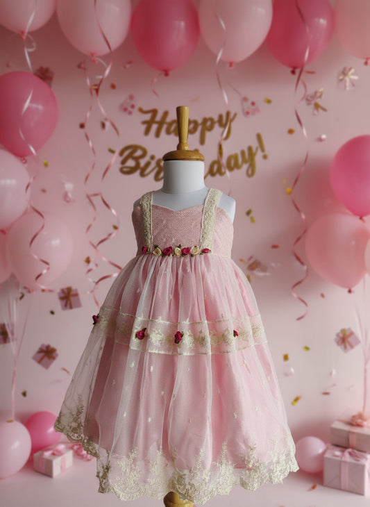 Pink dress with floral details on a mannequin against a white background with green leaves.