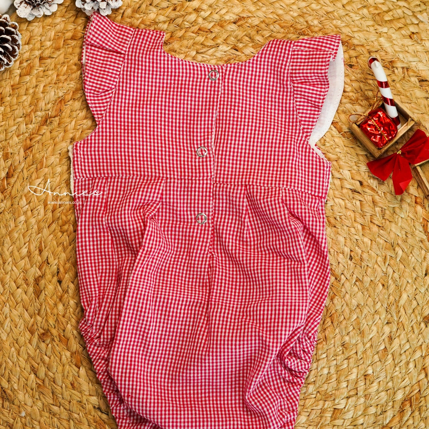 Red checkered baby romper on a woven surface with decorative items.