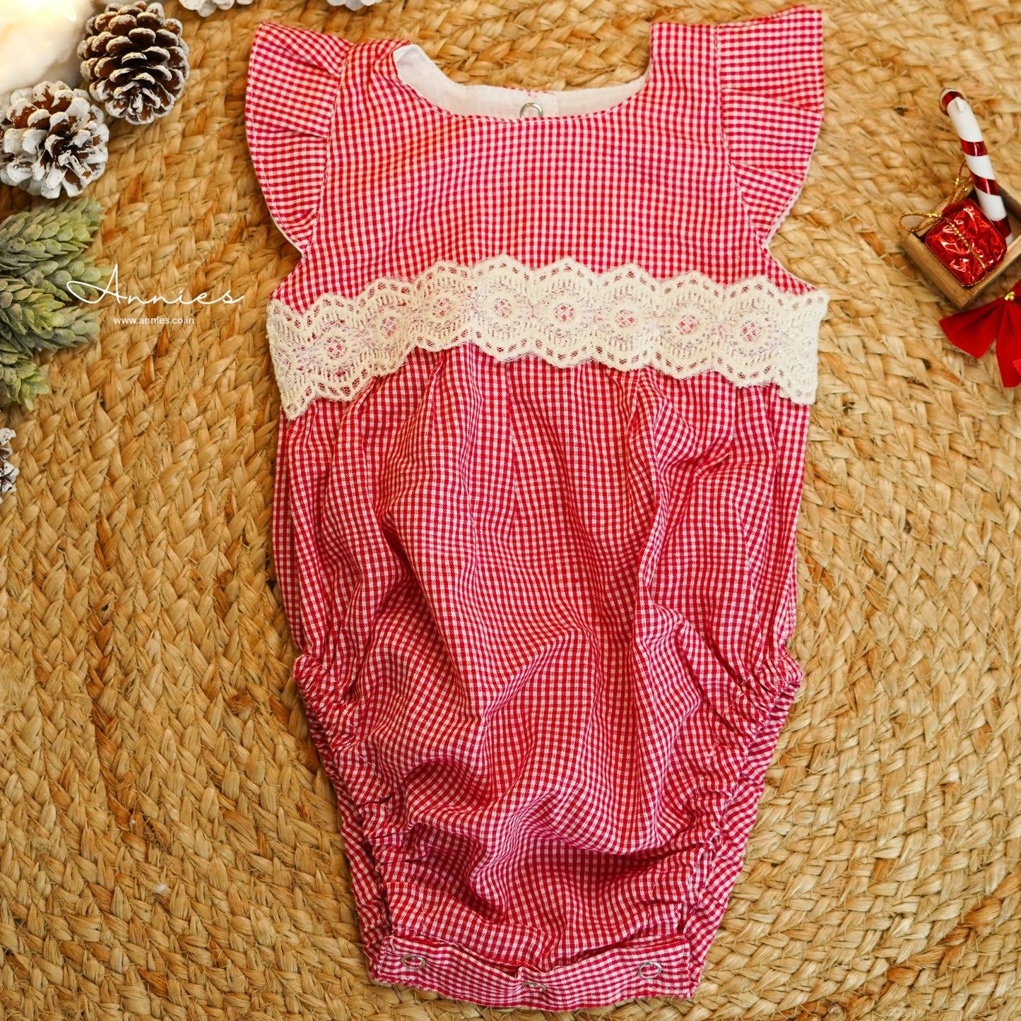 Red checkered baby romper with lace trim on a woven surface