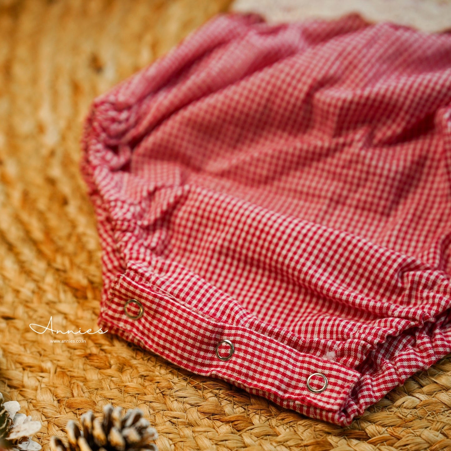 Red and white checkered baby bloomers on a woven surface