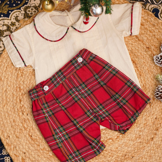 Red plaid shorts with a white shirt on a woven surface with Christmas decorations.