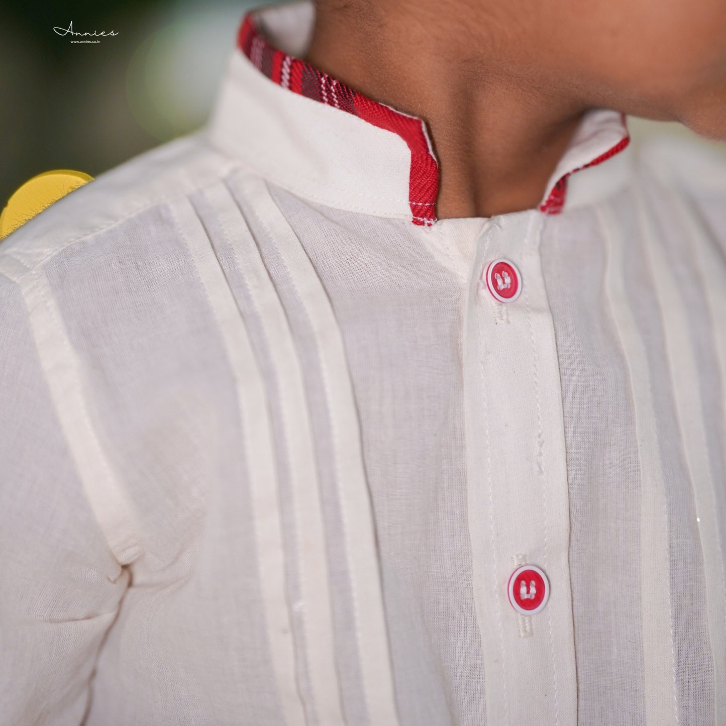 Close-up of a white shirt with red buttons and collar, blurred background