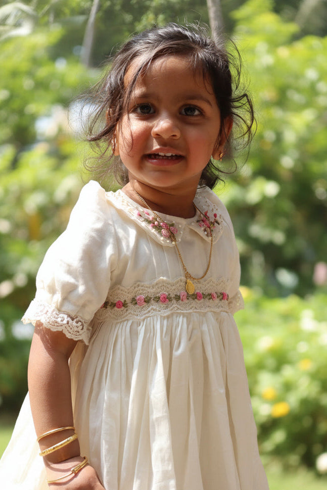 Young girl in a white dress standing outdoors with greenery in the background