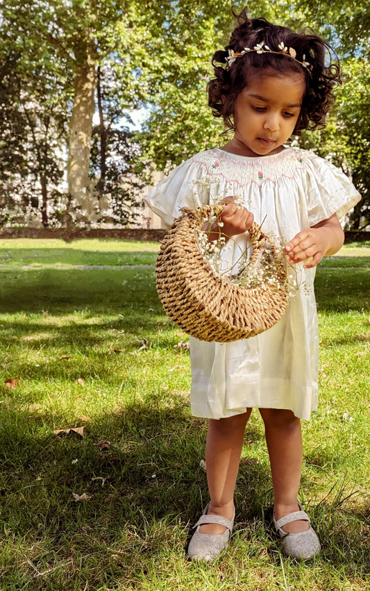 A baby girl wearing Snowy Smocked Bishop Dress by Annies