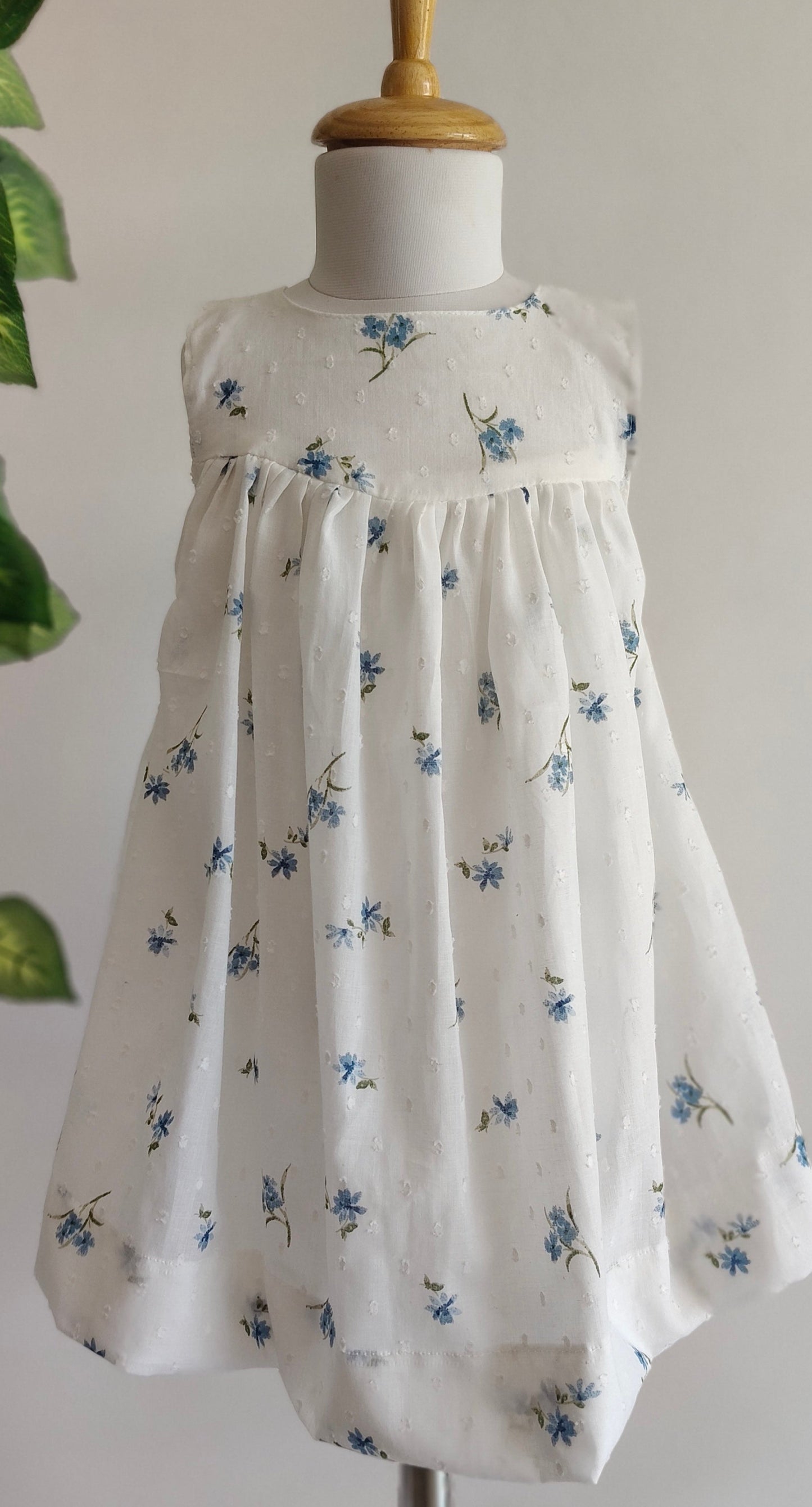 White dress with blue floral pattern on a mannequin against a neutral background