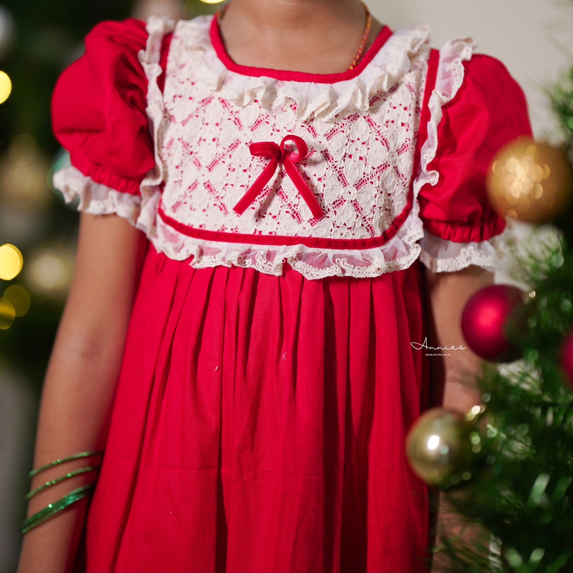 Red dress with white lace top worn by a child, Christmas tree in the background