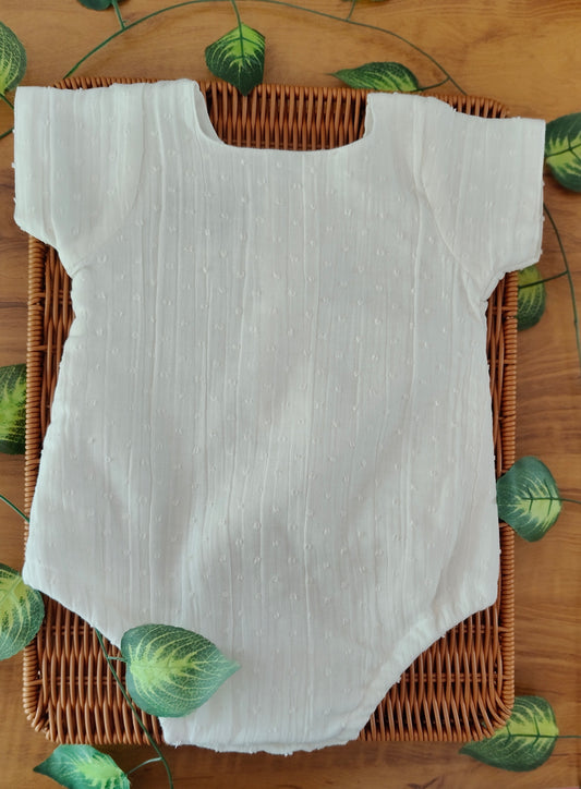 White baby onesie on a woven basket with a leaf patterned background