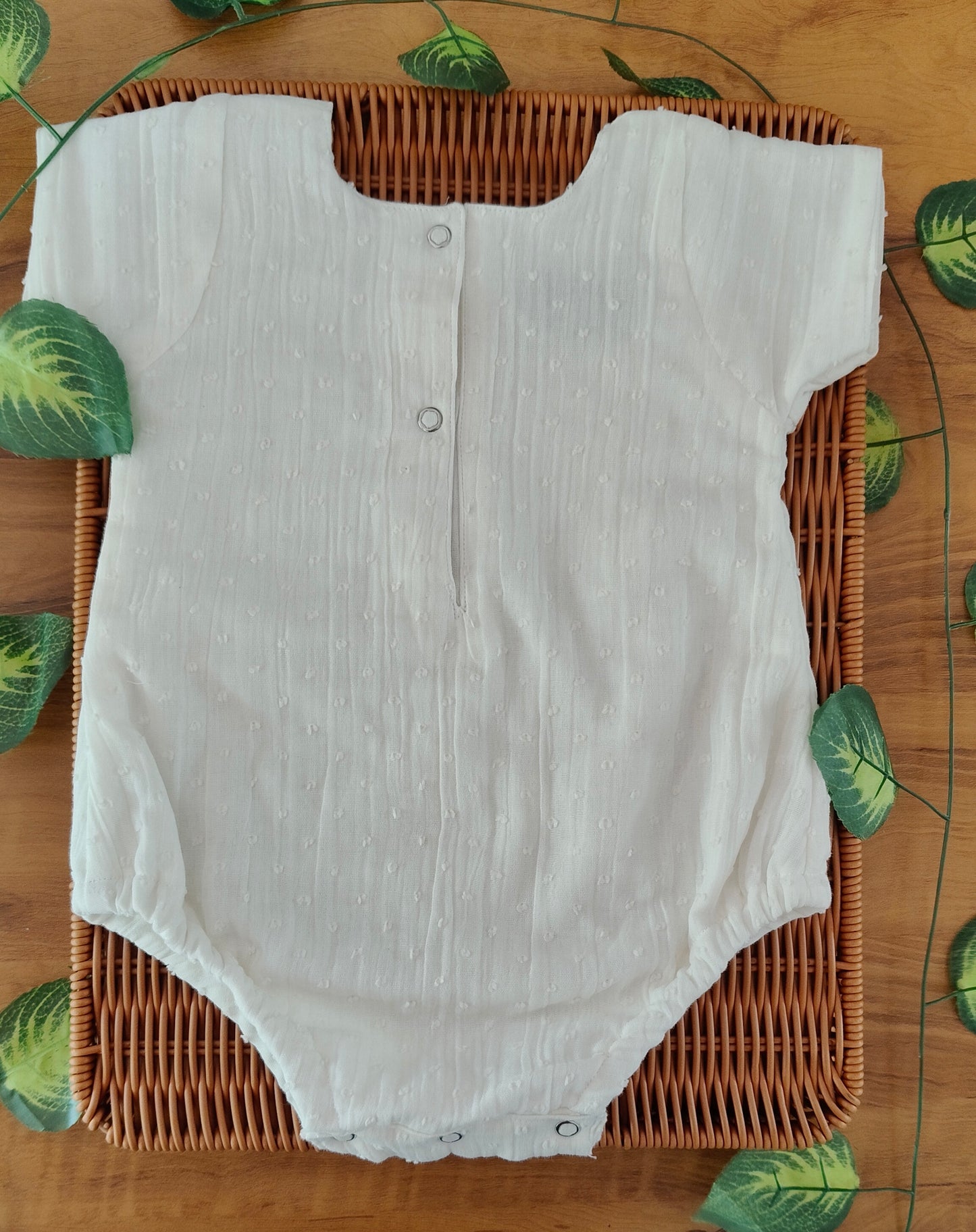 White baby onesie on a woven basket with a leaf patterned tablecloth